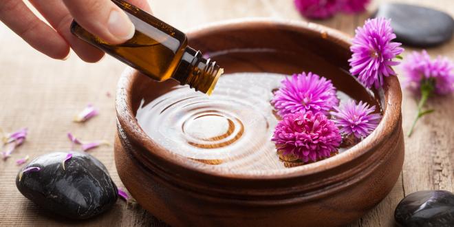 Essential oil being dripped in to a wooden dish for aromatherapy.