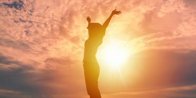 Happy woman raising hands up and beautiful sunrise in background.